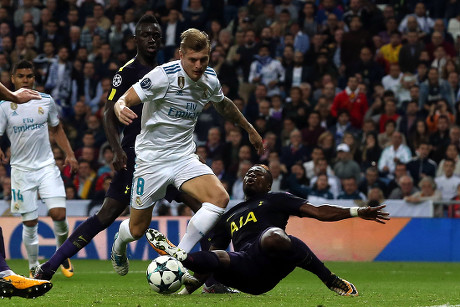 Toni Kroos - pomocnik - walczy o piłkę z zawodnikiem - Sergem Aurierem, który wykonuje wślizg podczas meczu na zatłoczonym stadionie.