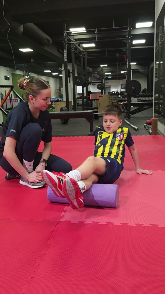 Fizjoterapeutka Futbol Elite pracuje z młodym piłkarzem na macie w sali treningowej