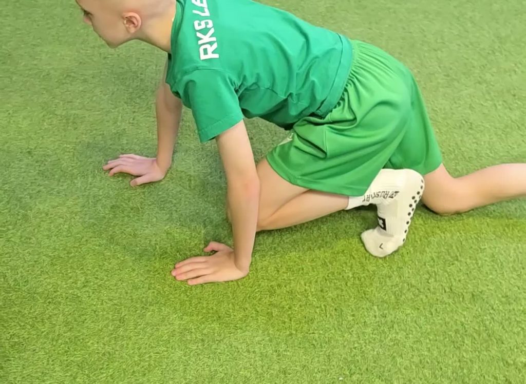 Ośmioletni piłkarz ćwiczy chód zwierzątka na treningu motorycznym w Futbol Elite